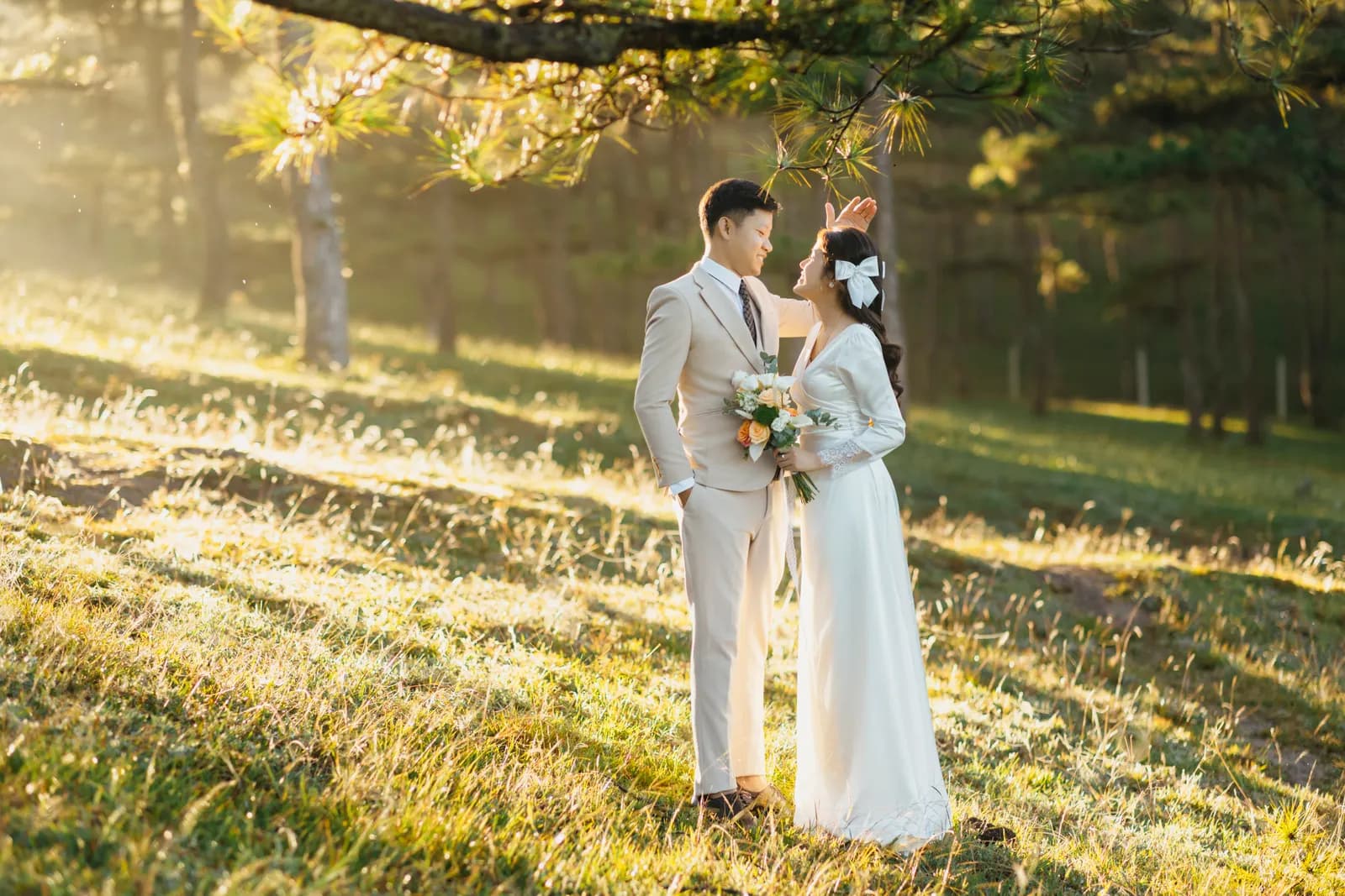 A bride and groom in ivory wedding attire in a sunlit meadow